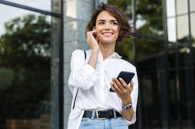 屋外に立っているイヤホンで幸せな若い女性