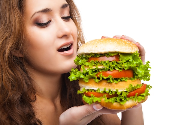 Happy young woman eating big yummy burger isolated on white background