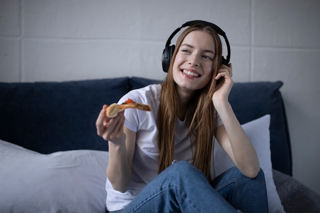 Photo happy young woman eating slice of hot pizza at home and watching film on laptop