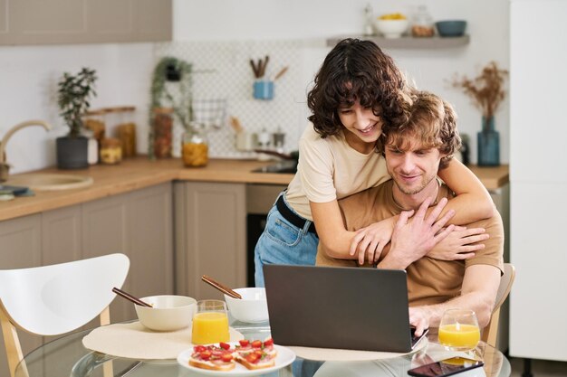 ビデオチャットでのコミュニケーション中に夫を抱きしめる幸せな若い女性