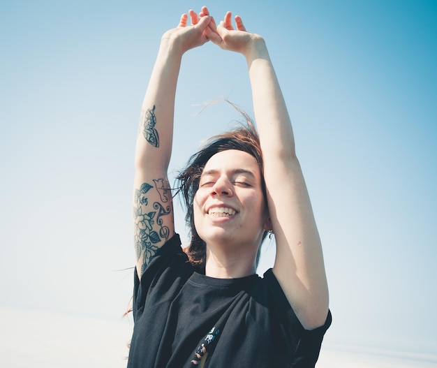 Happy young woman enjoying freedom raising arms to the sky while closing eyes Blowing hair and relax Liberty and future concept