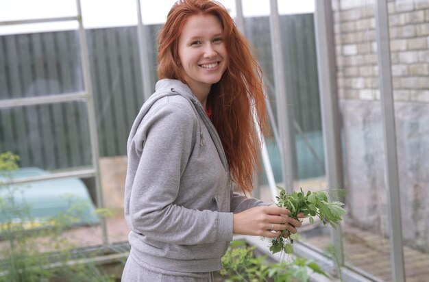 Photo happy young woman gardener harvesting greenery at her greenhouse at summer