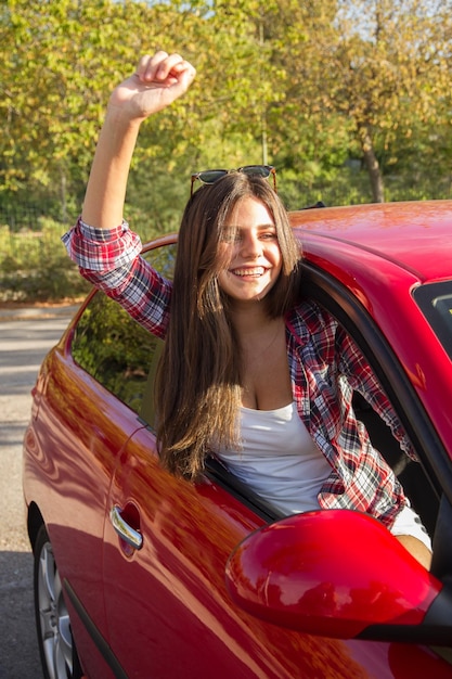 Happy young woman getting out of car window