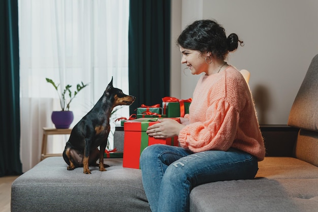 Счастливая молодая женщина дарит подарок своей собаке из подарочной коробки