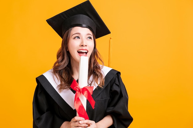 Happy young woman in graduation gowns holding diploma and looking away