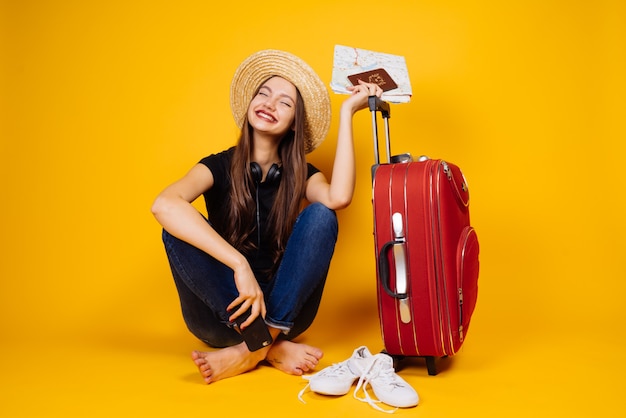 Happy young woman in a hat sends on vacation, on a journey, holds plane tickets, and a big red suitcase