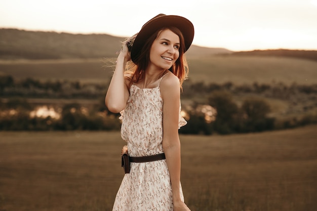 Happy young woman in hat standing in summer field