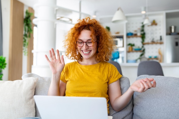 Foto giovane donna felice che si diverte a fare videochiamate utilizzando il laptop nella sua casa agitando la mano in videoconferenza chiamando il computer portatile siediti sul divano a distanza impara lo zoom riunione virtuale online a casa