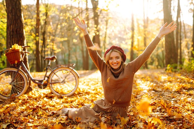 秋の公園で葉を楽しんで幸せな若い女性