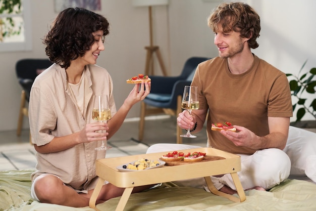 Счастливая молодая женщина и ее муж держат бутерброды и бокалы с шампанским
