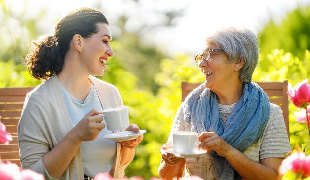 Happy young woman and her mother drinking tea in summer morning Family sitting in the garden