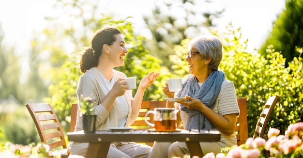 Happy young woman and her mother drinking tea in summer morning Family sitting in the garden