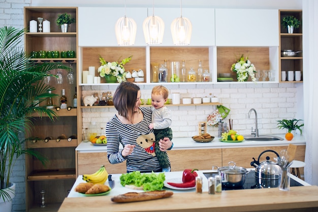 Happy young woman holding a 1 year old child and cooking together in the kitchen