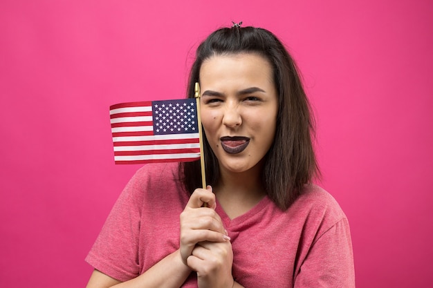 Happy young woman holding American flag against a studio pink background