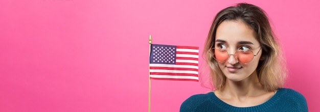 Happy young woman holding American flag against a studio pink background