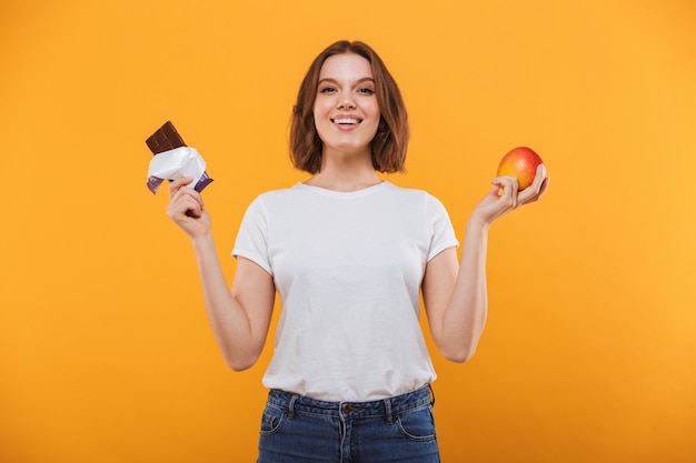 Happy young woman holding apple and chocolate.