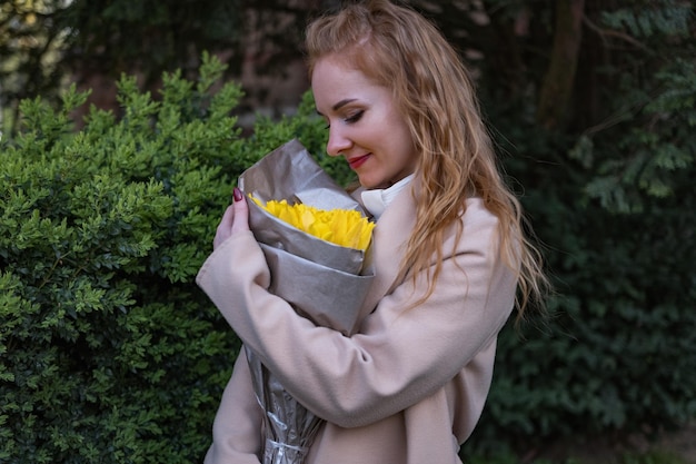 写真 黄色いチューリップの花束を握っている幸せな若い女性 公園で花を持った笑顔の女の子が 誰かを待っている 最初のデート