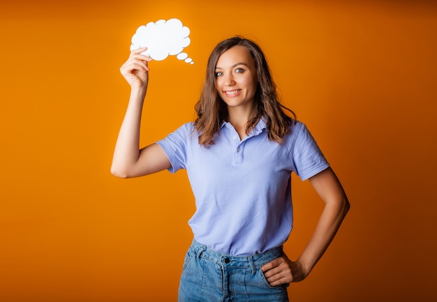 Happy young woman holding empty speech bubble on yellow background.