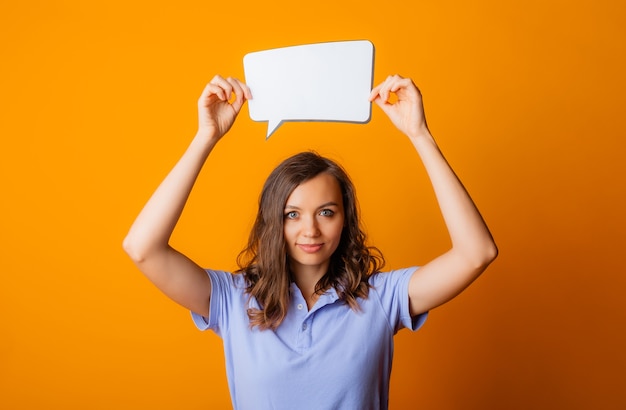 Happy young woman holding empty speech bubble on yellow background.