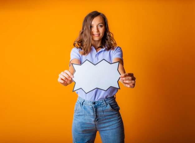 Happy young woman holding empty speech bubble on yellow background.