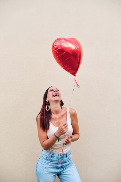 Happy young woman holding a heart balloon and smiling while standing outdoors on the street.