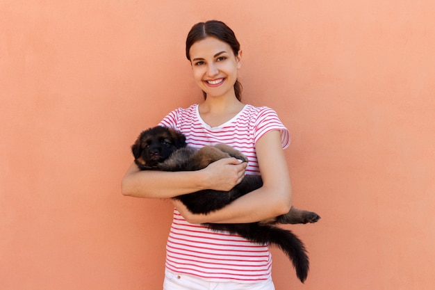happy young woman holding her pet puppy on orange background