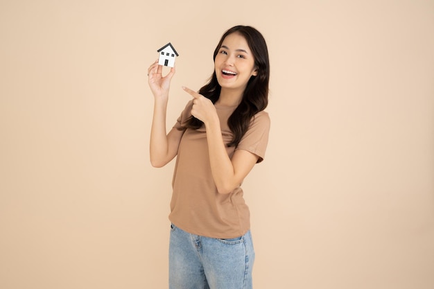 Happy young woman holding a house model standing in the studio