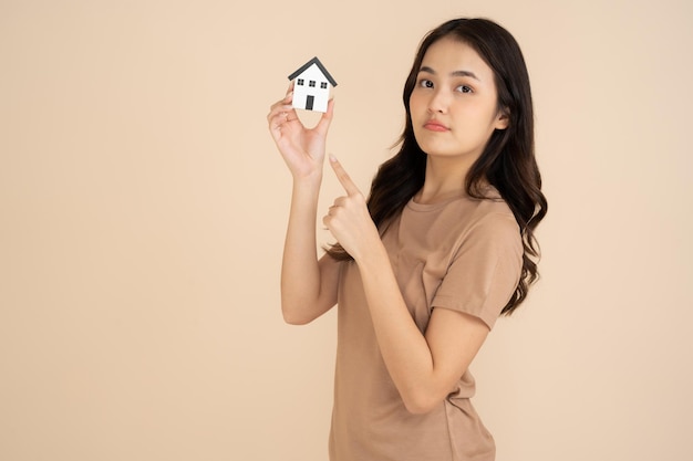 Happy young woman holding a house model standing in the studio