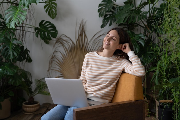 Счастливая молодая женщина, держащая ноутбук на коленях, визуализируя хорошее будущее, наслаждаясь свободным временем с ноутбуком