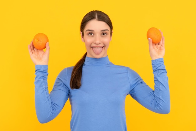 Happy young woman holding orange citrus fruit on yellow background organic
