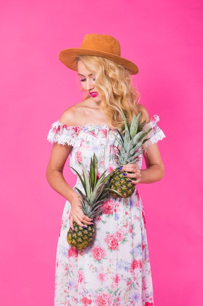 Giovane donna felice che tiene un ananas su una parete rosa