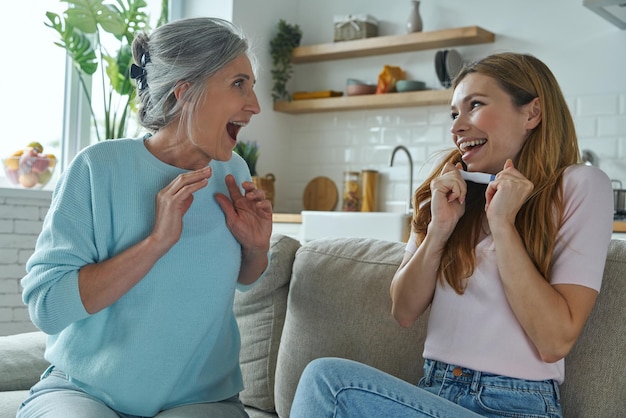 Photo happy young woman holding pregnancy test while sitting with her mother on the couch at home