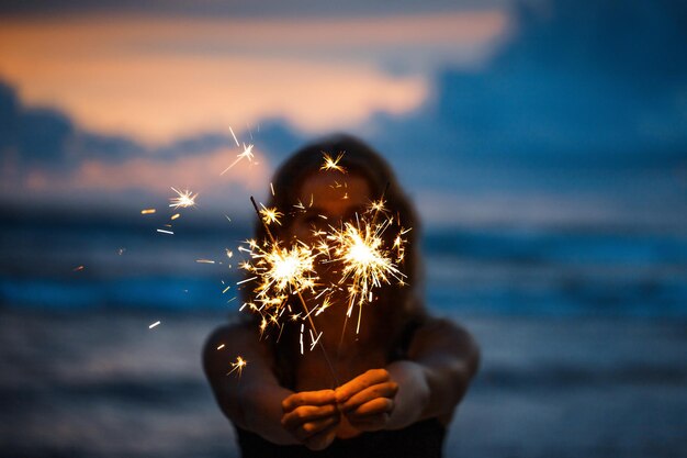 Foto felice giovane donna che tiene sparkler festeggiare il capodanno sulla spiaggia