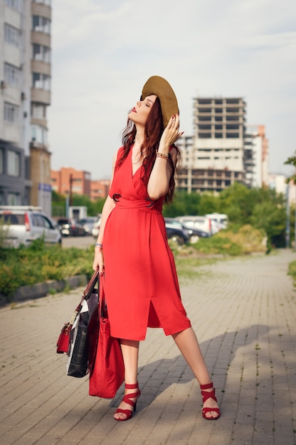 Una giovane donna felice, con in mano un cappello largo, posa nel parco cittadino in estate