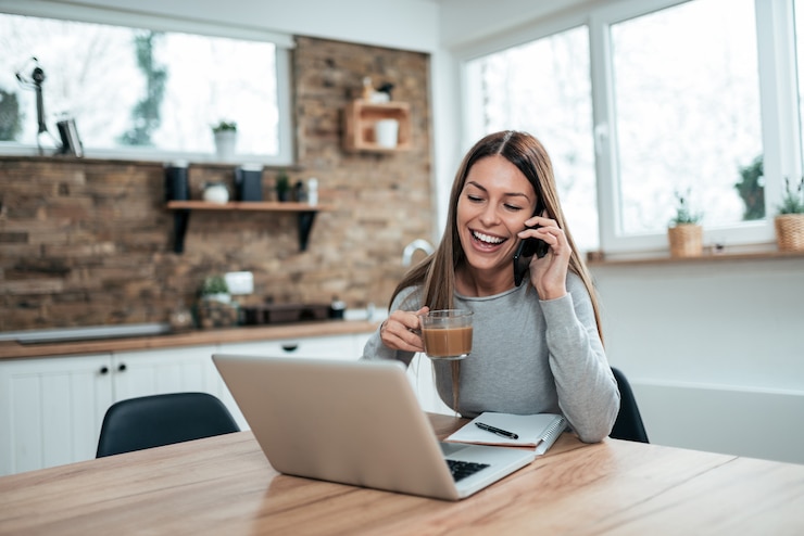 Photo happy young woman at home, talking on mobile phone and using laptop, drinking hot chocolate.