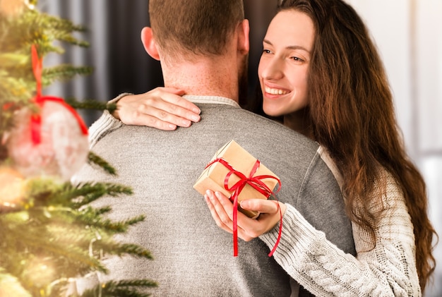 Happy young woman hugs man and holds gift box in hand
