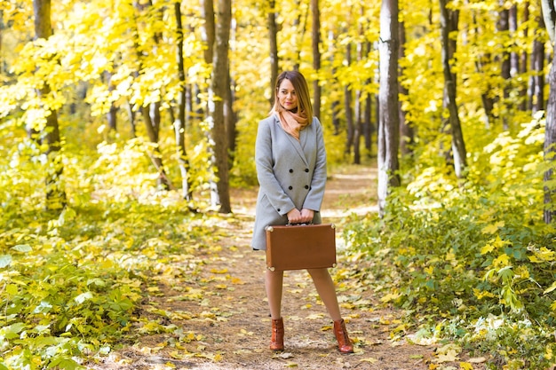 Happy young woman is going on a trip with retro suitcase on a forest