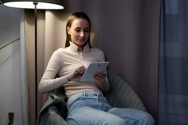 幸せな若い女性は ⁇ 現代的なタブレットガジェットを使った快適な椅子で自宅で休息しています ⁇ 