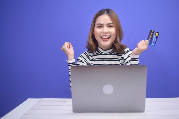 La giovane donna felice sta facendo acquisti online tramite laptop, in possesso di carta di credito credit