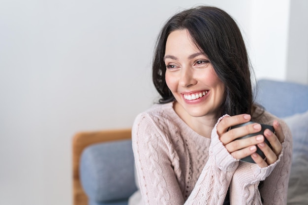 A happy young woman is sitting at home on the couch and looking at the camera portrait of a cozy