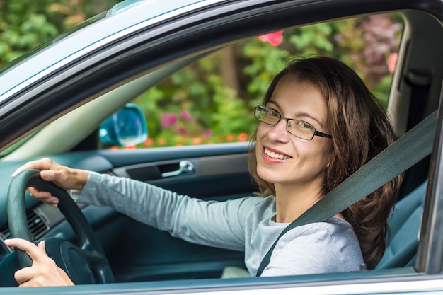 A happy young woman is sitting at the wheel of a car