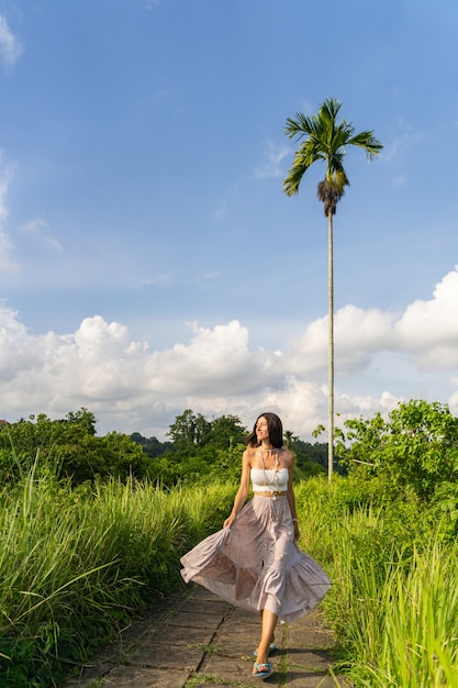 Happy young woman is spending sunny day in tropics by walking in rice plantations. Travelling concept