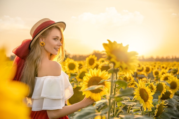 Happy young woman is in sunflower field at sunset