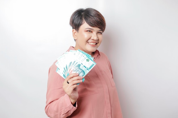 A happy young woman is wearing pink shirt and holding cash money in Indonesian rupiah isolated by white background