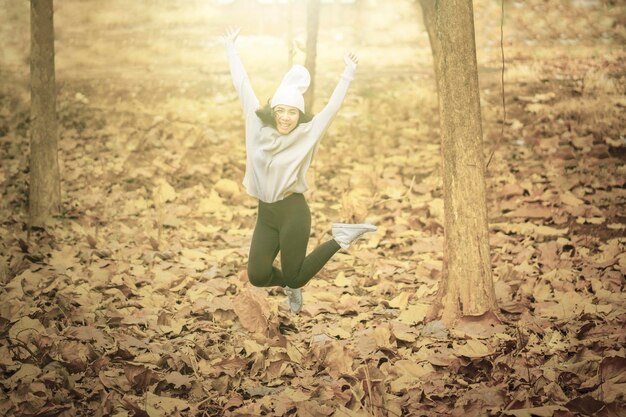 写真 秋の公園でジャンプする幸せな若い女性