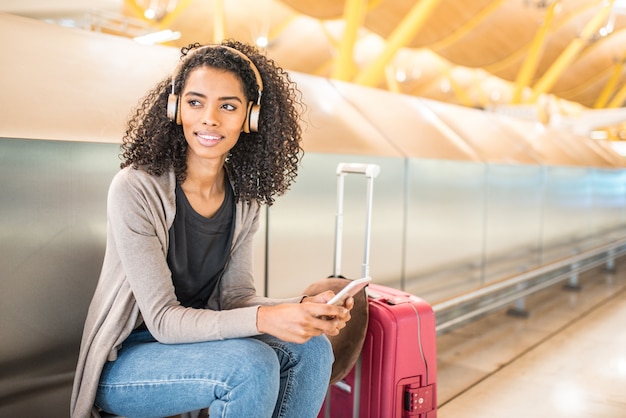 Счастливая молодая женщина прослушивания музыки с наушниками и мобильным телефоном в аэропорту