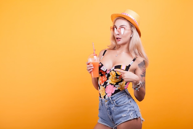 彼女は黄色の背景の上のスタジオでセクシーだと思って夏の新鮮なオレンジジュースを見て幸せな若い女性