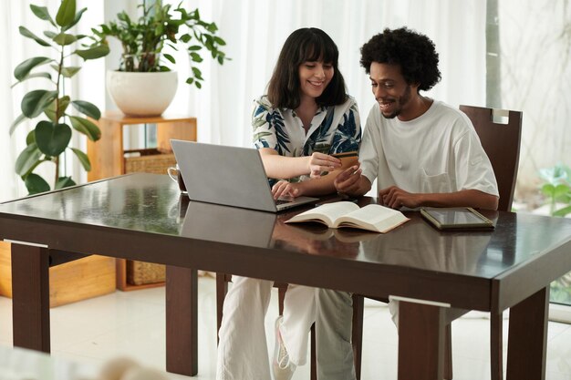 Photo happy young woman looking at number of credit card held by her boyfriend while sitting next to him and entering banking data