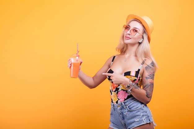 Happy young woman looking at summer fresh orange juice thinking she's sexy in studio over yellow background