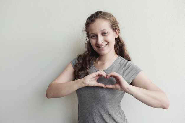 La giovane donna felice che fa le sue mani nel cuore modella